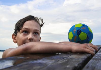 Portrait of boy with ball in water against sky