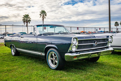 Vintage car parked by palm trees against sky