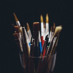 Close-up of paintbrushes in glass against black background