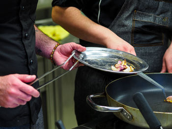 Chef cooking and grilling onions and a golden potato on a pan in a professional restaurant kitchen.