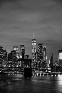 Illuminated buildings by river against sky in city