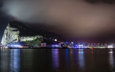 Illuminated city by sea against sky at night