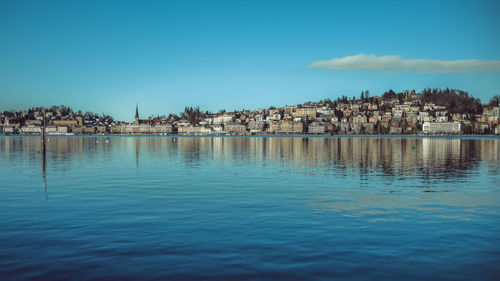 Scenic view of lake by buildings against blue sky