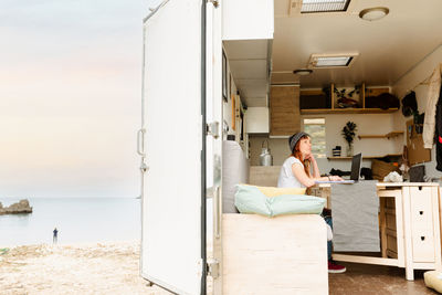 Side view of focused female traveler sitting at table in truck and taking notes while working on project remotely and leaning on hand