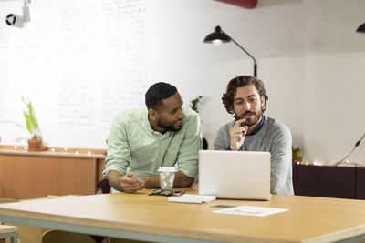 Businessman discussing with colleague while using laptop computer in office