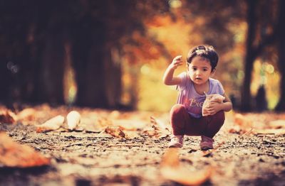 Girl gesturing while crouching on field during autumn