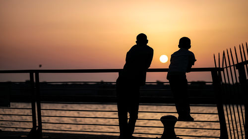 Silhouette people standing on bridge against sky during sunset