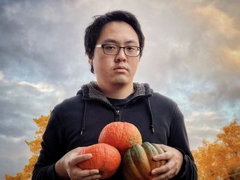 Portrait of young man holding ice cream against sky