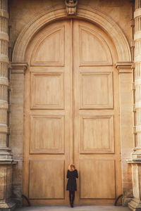 Rear view of woman standing against closed wooden door of historic building