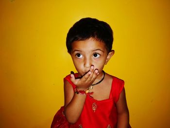 Girl covering mouth with hand against yellow background