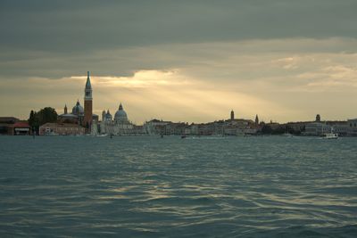 View of buildings by canal against sky in city