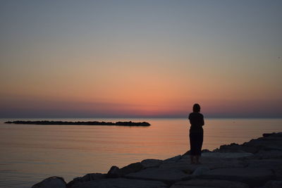 Rear view of woman looking at sea against sky during sunset