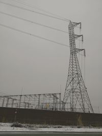 Low angle view of electricity pylon against sky during winter