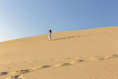 Woman walking on sand dune against clear sky
