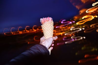 Close-up of hand holding ice cream cone at night