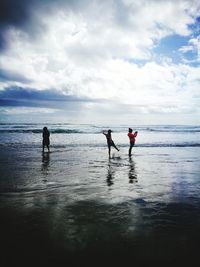 People playing on beach against cloudy sky