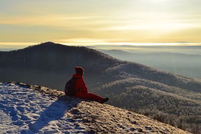 Rear view of man sitting on mountain during winter