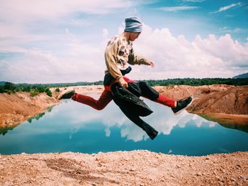 Side view of man jumping over lake against sky