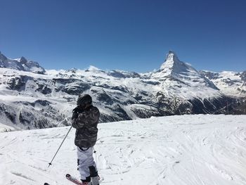 Man skiing on snowcapped mountain against blue sky