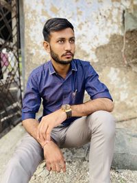 Young man looking away while sitting on wall