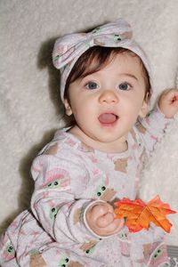 Portrait of cute baby girl sitting on bed at home