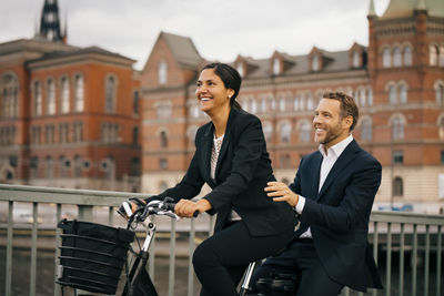 Smiling businesswoman and businessman traveling on bicycle in city