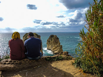 Rear view of couple sitting at beach against sky