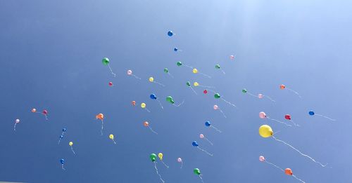 Low angle view of balloons flying in sky during sunny day