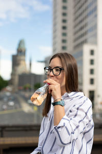 Young woman drinking juice sitting against building in city