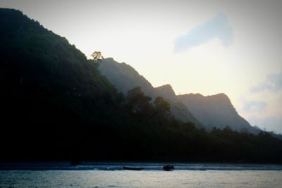 Scenic view of river by silhouette mountain against sky