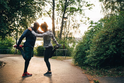 Full length of male and female athletes stretching legs while standing on road in park