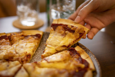 Close-up of hand holding  a slice of hot delicious pizza on table
