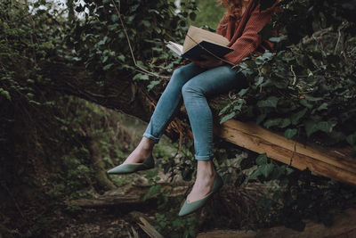 Low section of woman on tree trunk in forest