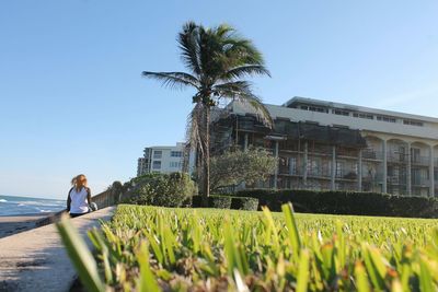 Rear view of woman walking at sea shore by building against clear sky