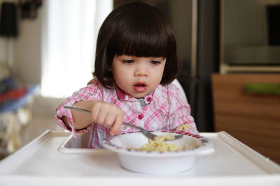 Close-up of cute baby girl eating food while sitting on high chair at home