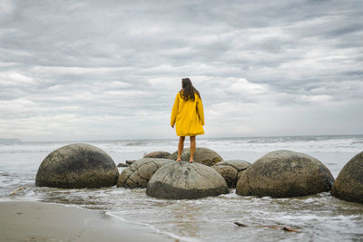 Rear view of man standing on rock by sea against sky