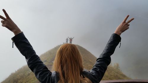 Rear view of woman gesturing peace sign against friends on mountain