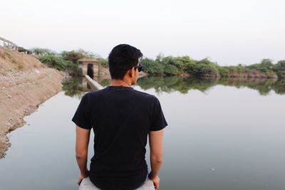 Rear view of man standing in lake against clear sky