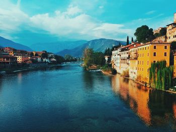 Buildings by river against sky in town