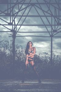 Portrait of young woman in lingerie standing at park against cloudy sky