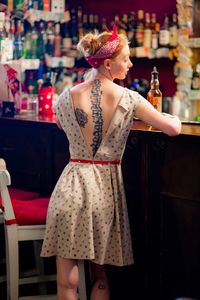 Rear view of woman with tattoo on back standing at bar counter