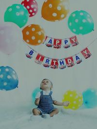 Baby boy sitting with colorful balloons at home during birthday