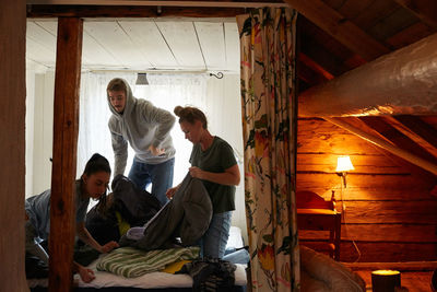 Female and male friends folding blankets on bed in cottage