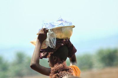Close-up of woman carrying container against sky