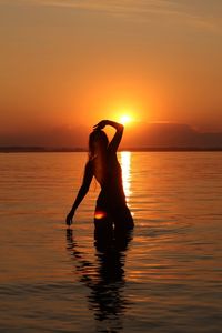 Silhouette woman in sea against sky during sunset