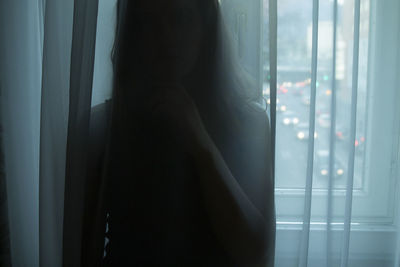 Rear view of woman looking through curtain