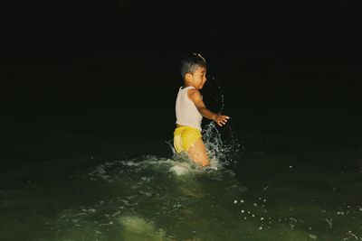 Playful boy dancing in lake against sky during night