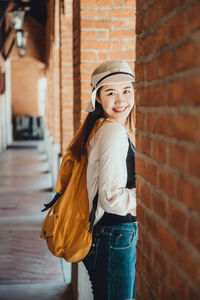 Portrait of smiling young woman standing against brick wall