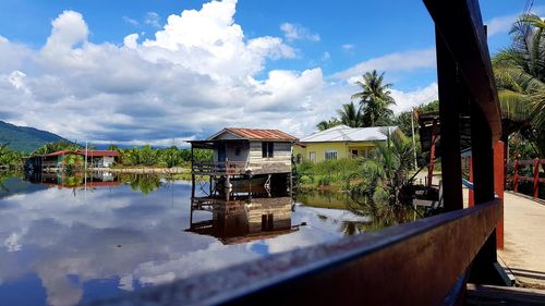 House by lake and buildings against sky