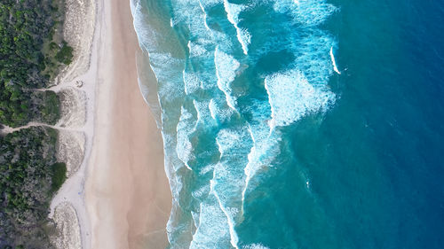 Foamy ocean waves roll and approach sandy beach. majesty turquoise seascape. top view from drone.